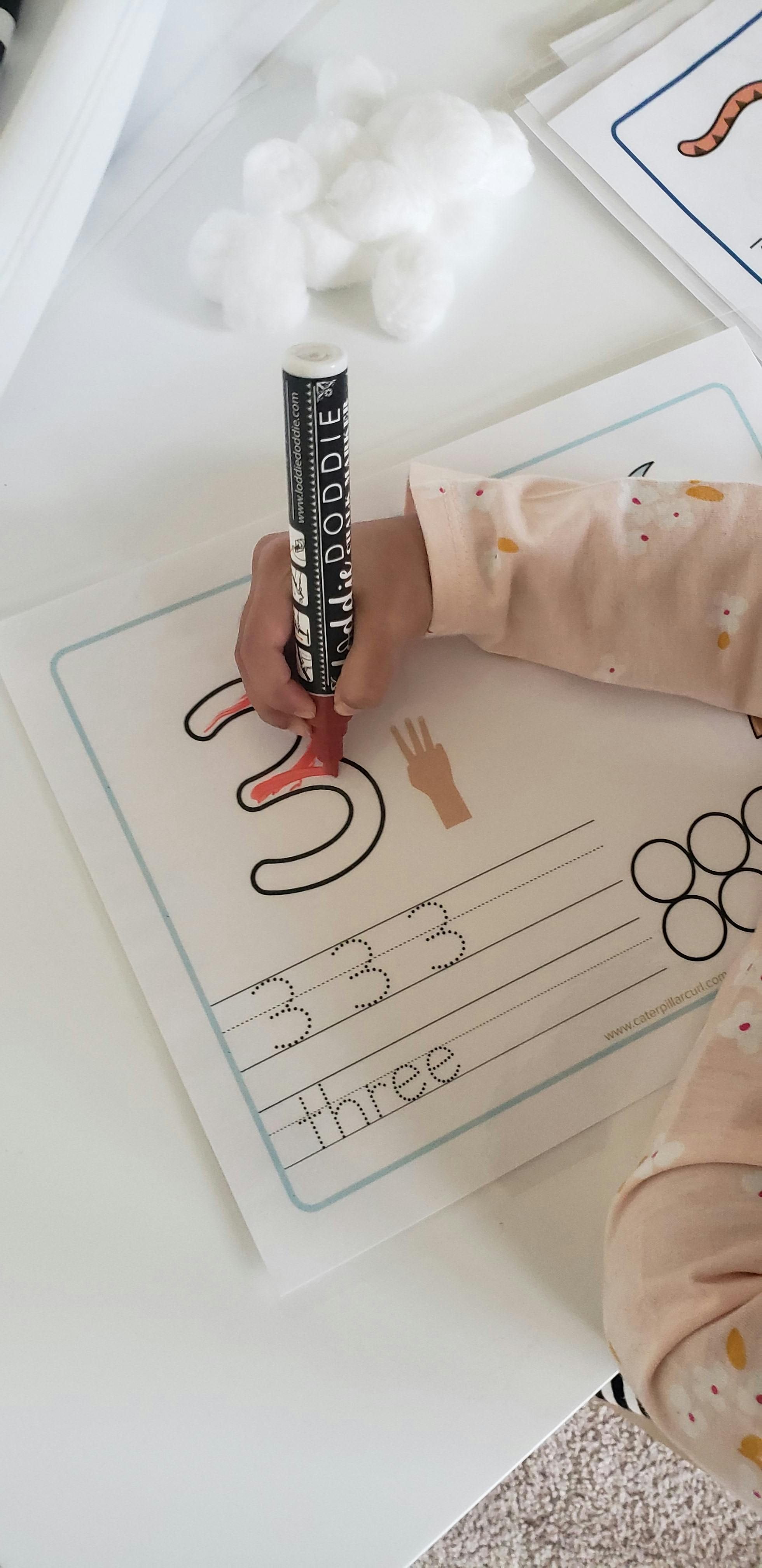 Child's hand holding a marker and tracing the number three
