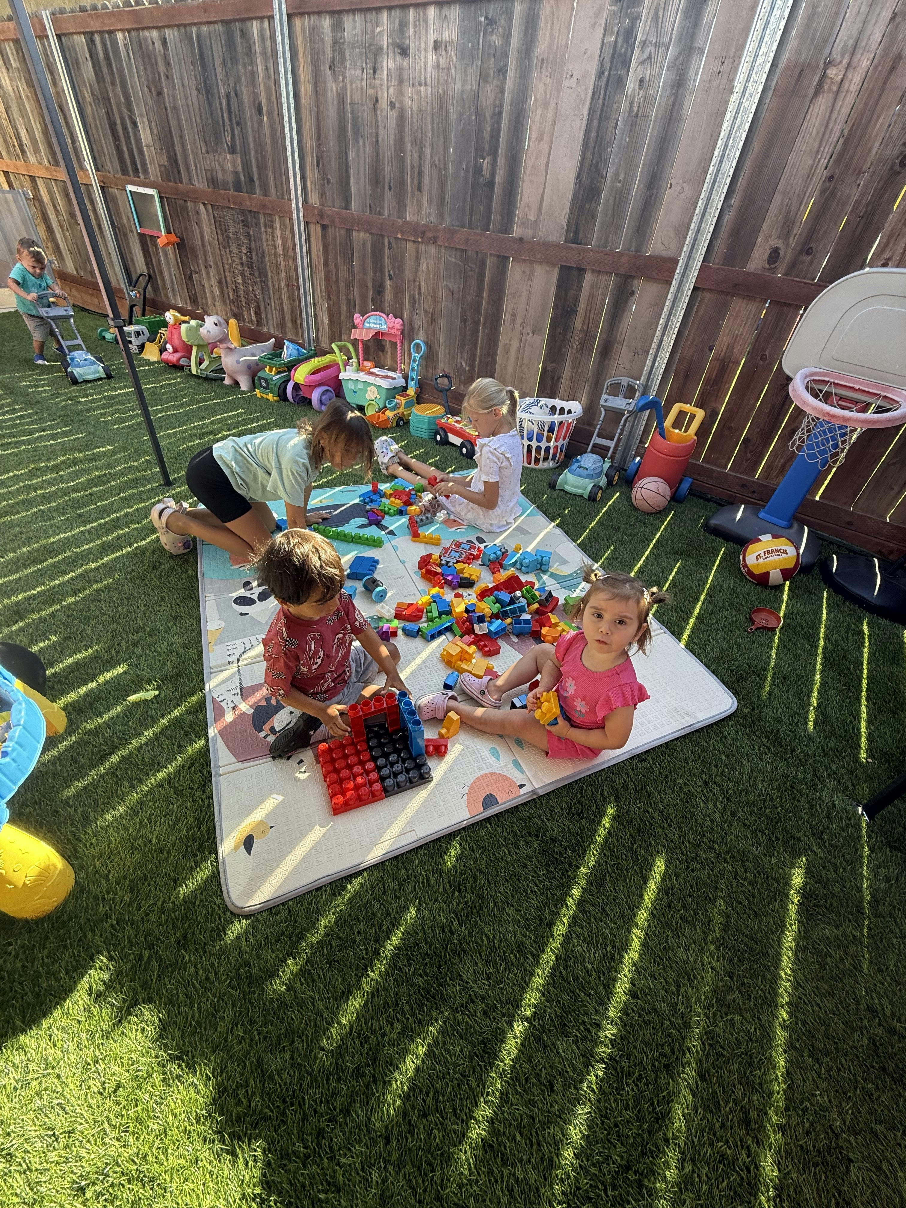 Children playing with colorful blocks on a mat in an outdoor area