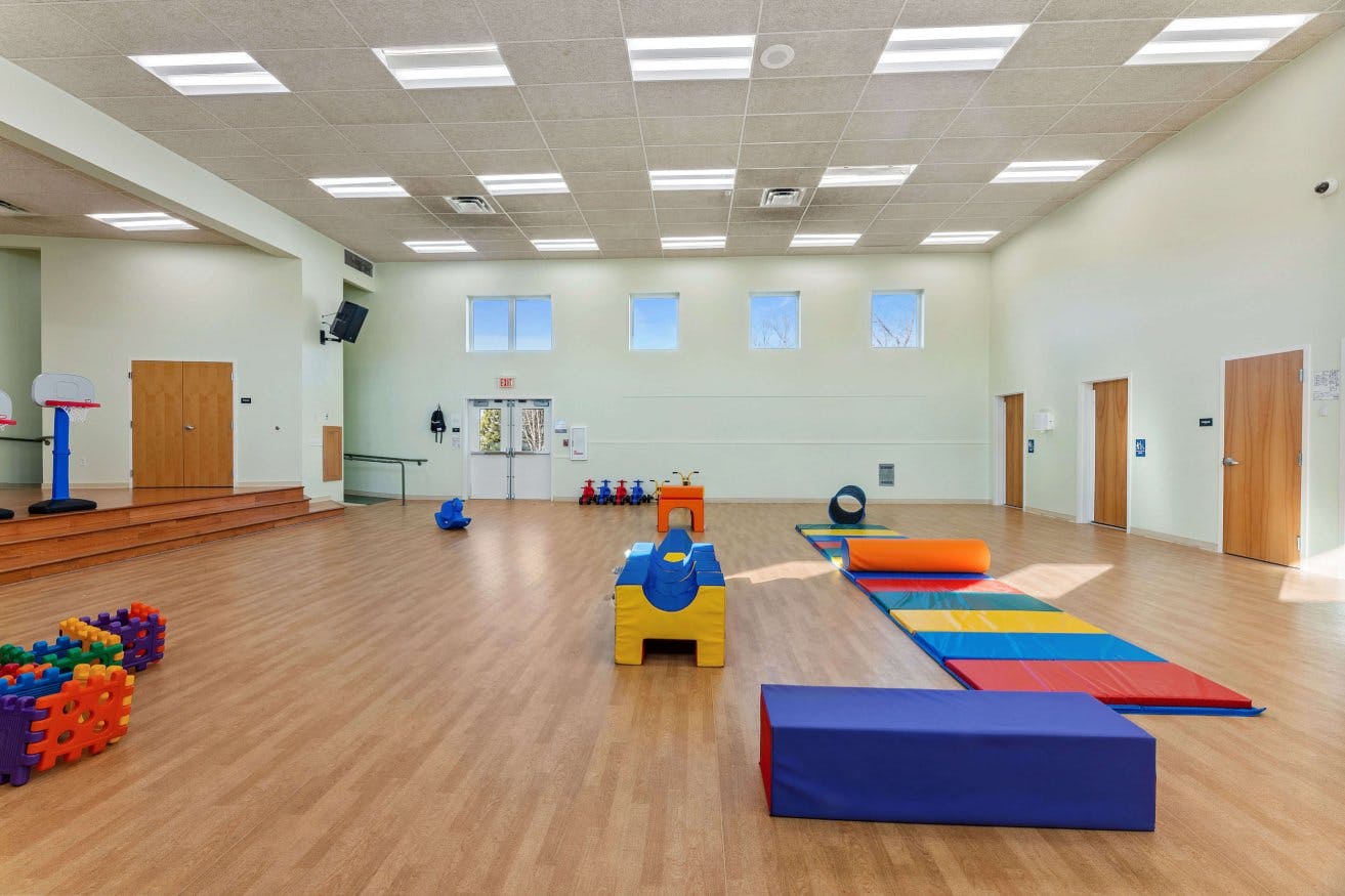 Empty children's play room with colorful mats, soft play equipment, and small basketball hoops