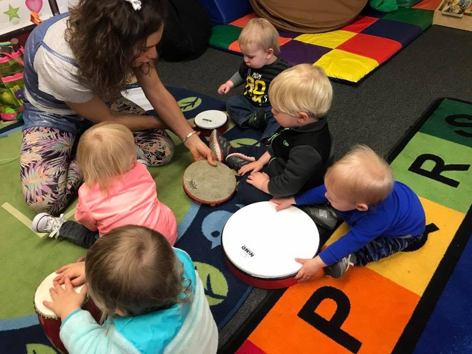 Person and multiple children playing drums on a colorful rug