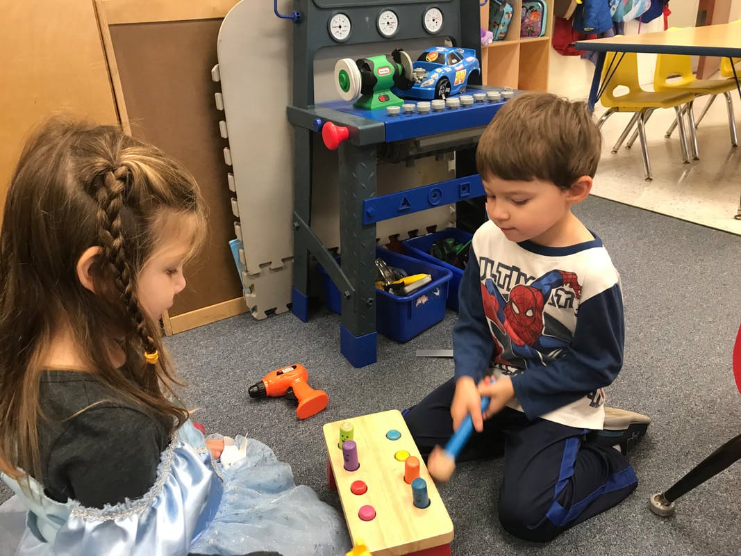 Two children playing with toys on the floor in a classroom