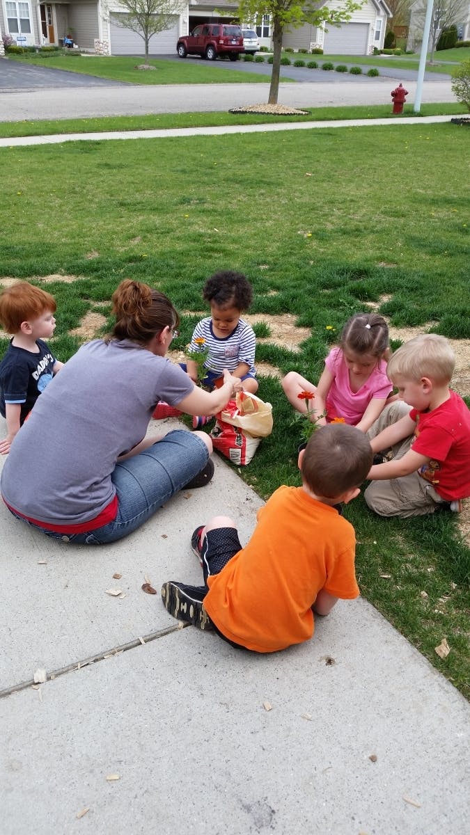 Adult and children sitting on grass and sidewalk, looking at items in a bag