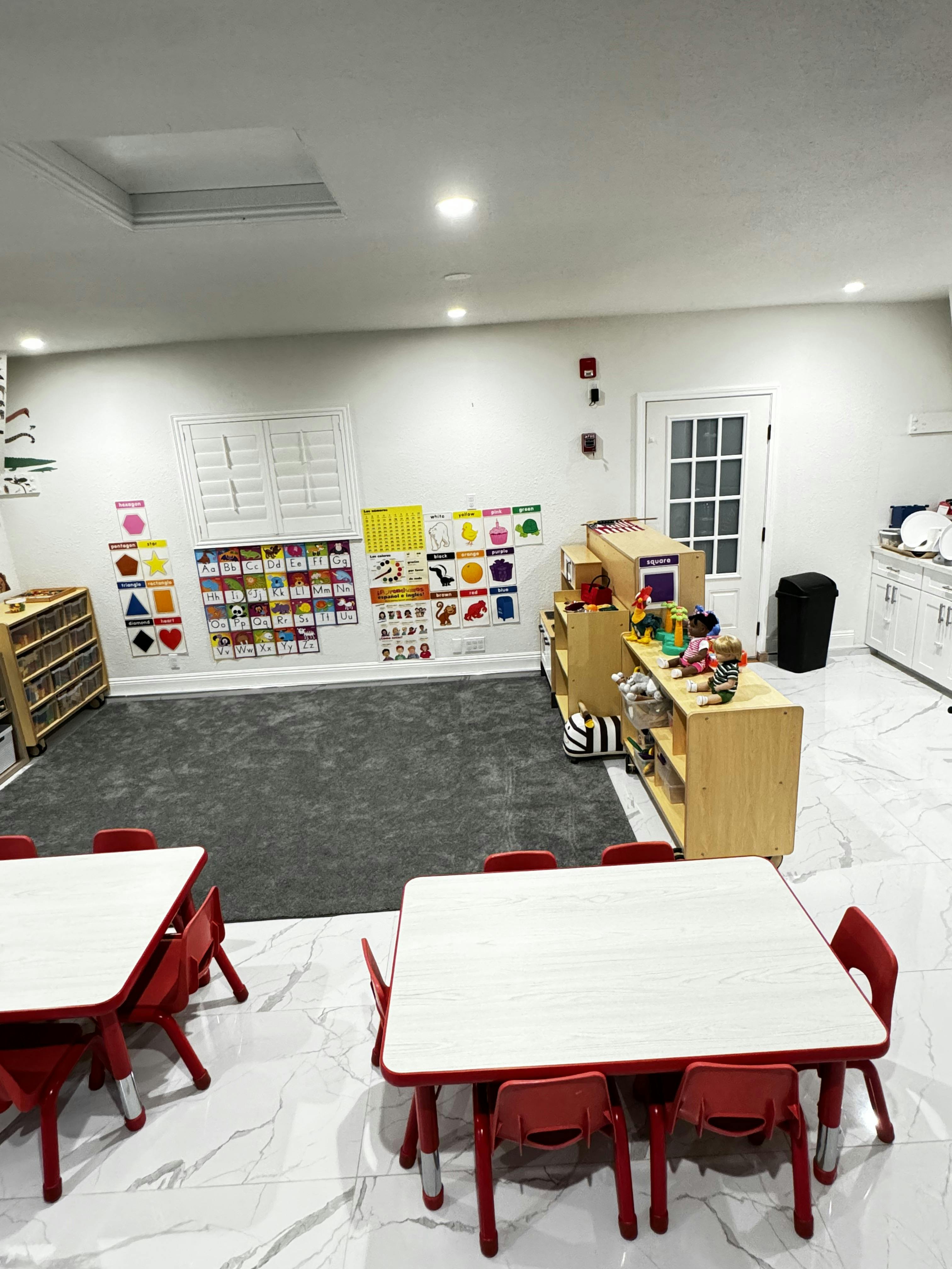 Classroom with small red tables and chairs, educational posters, and play furniture