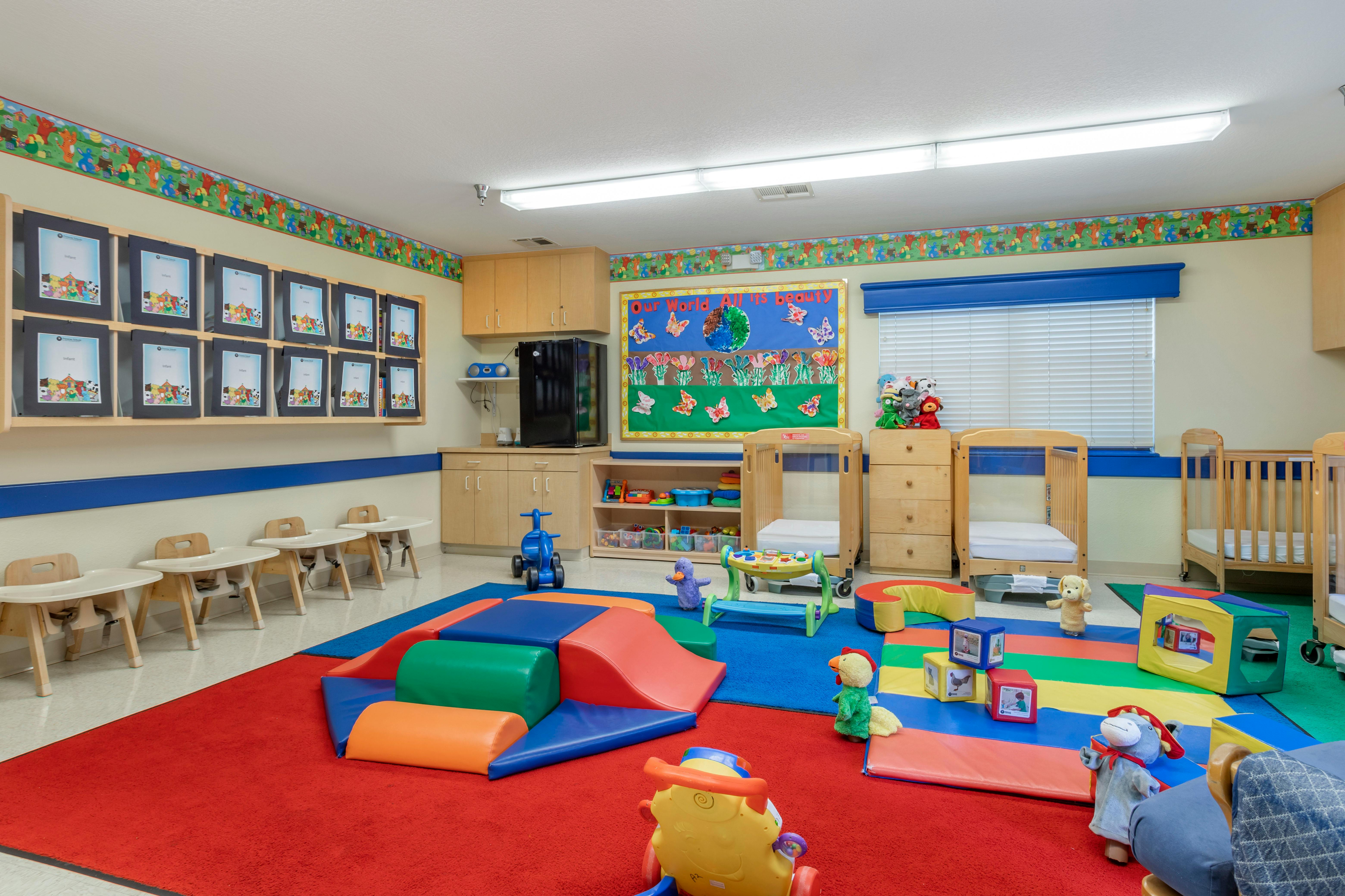 An infant daycare room with play mats, cribs, high chairs, and wall decor