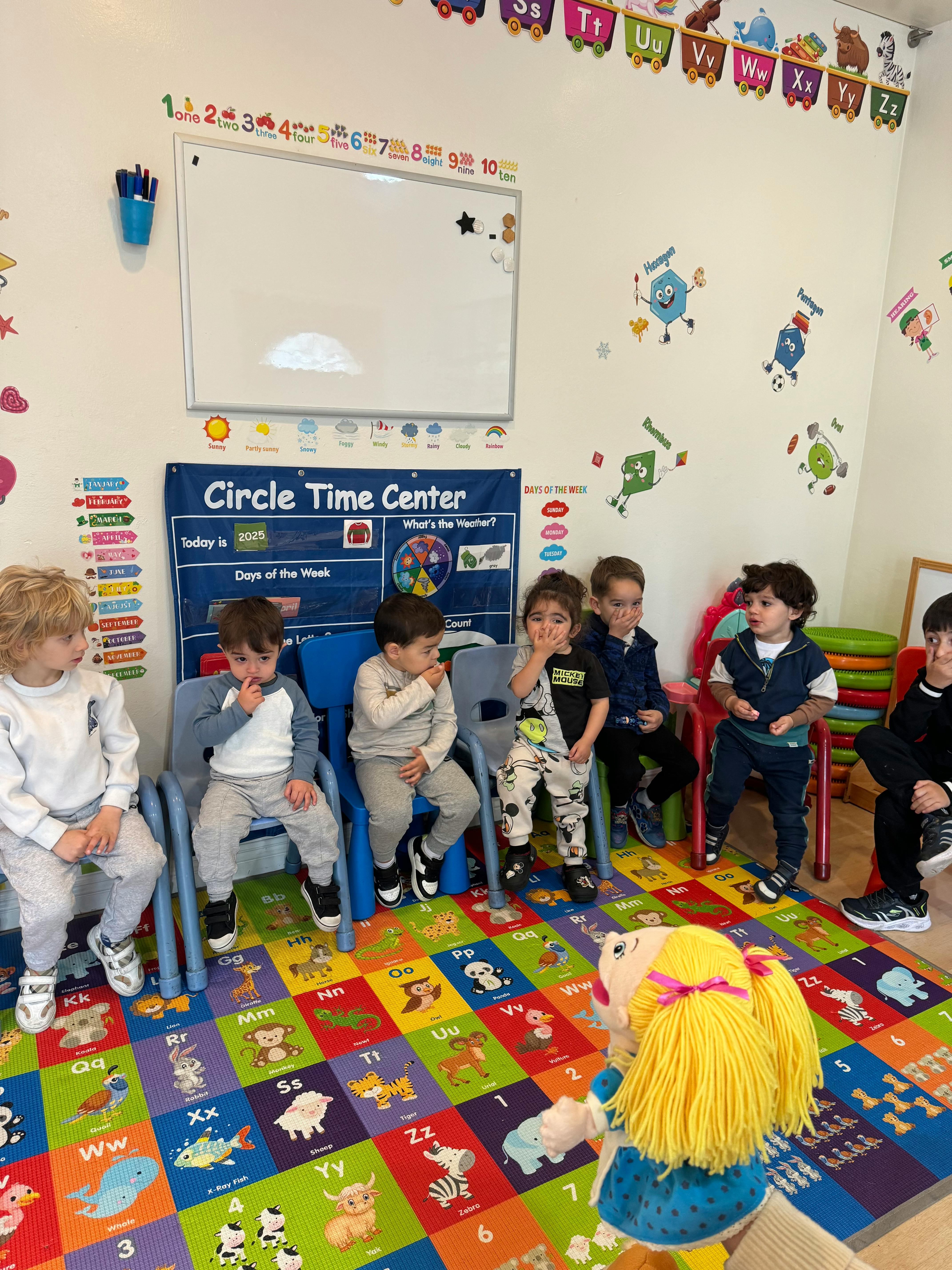 Children sitting in chairs in a classroom with a puppet