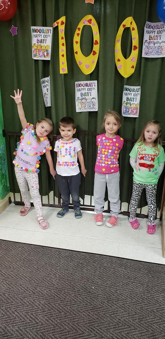 Four children standing in front of a "Hooray Happy 100th Day" banner