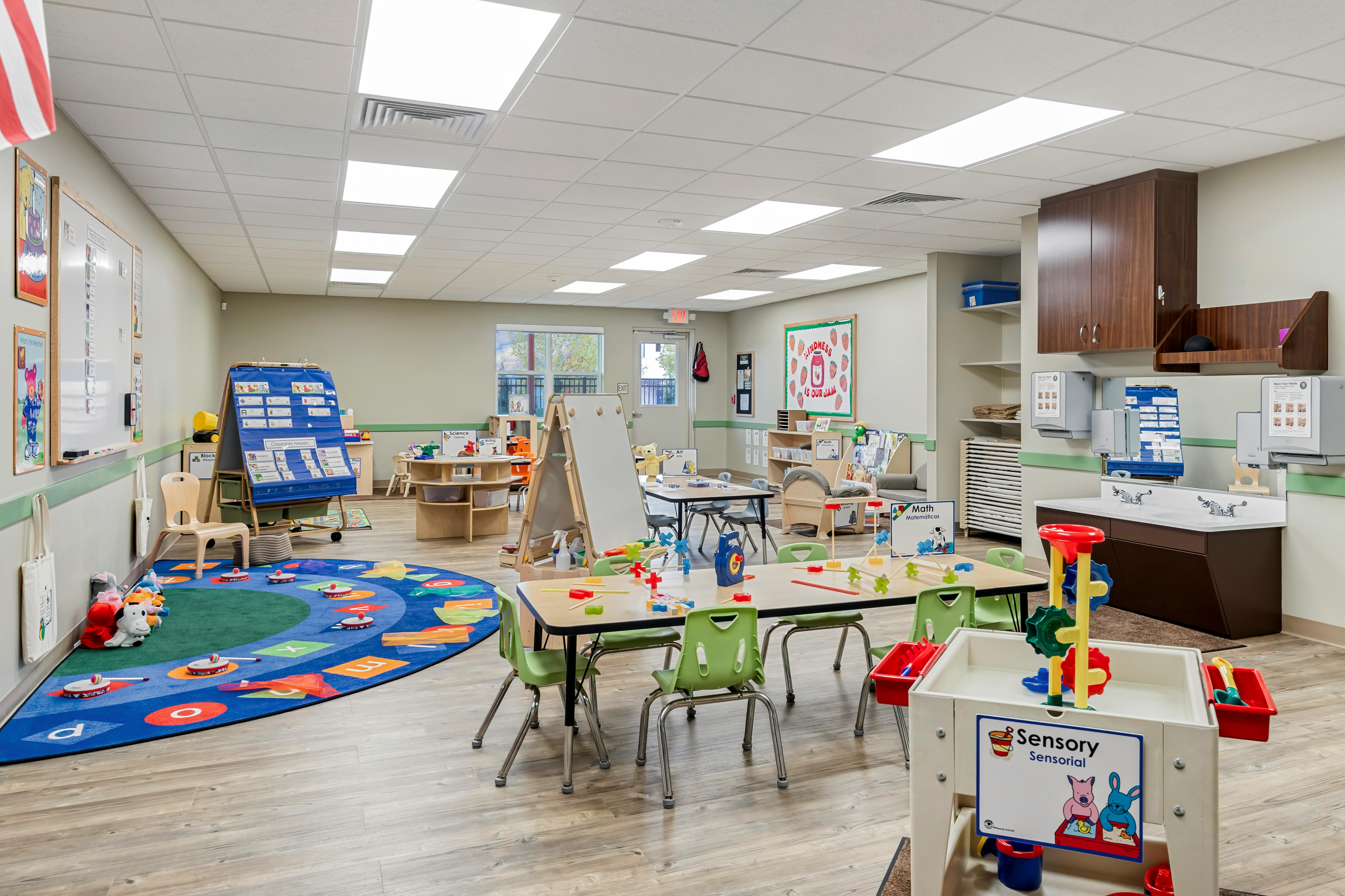 An empty early childhood classroom with activity tables, chairs, and play areas