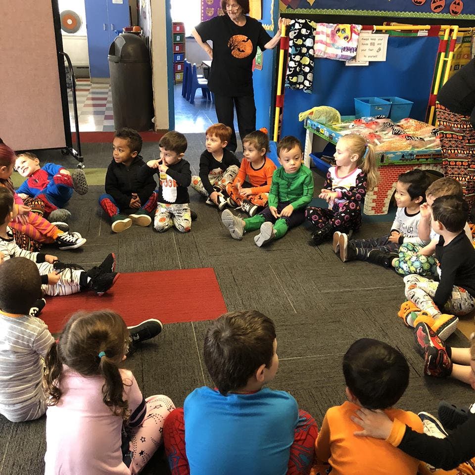 Adult standing in a classroom with children sitting in a circle on the floor