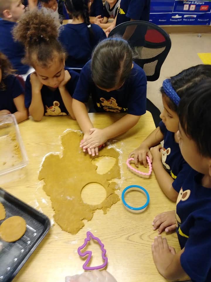 Children using cookie cutters on dough at dough at a table