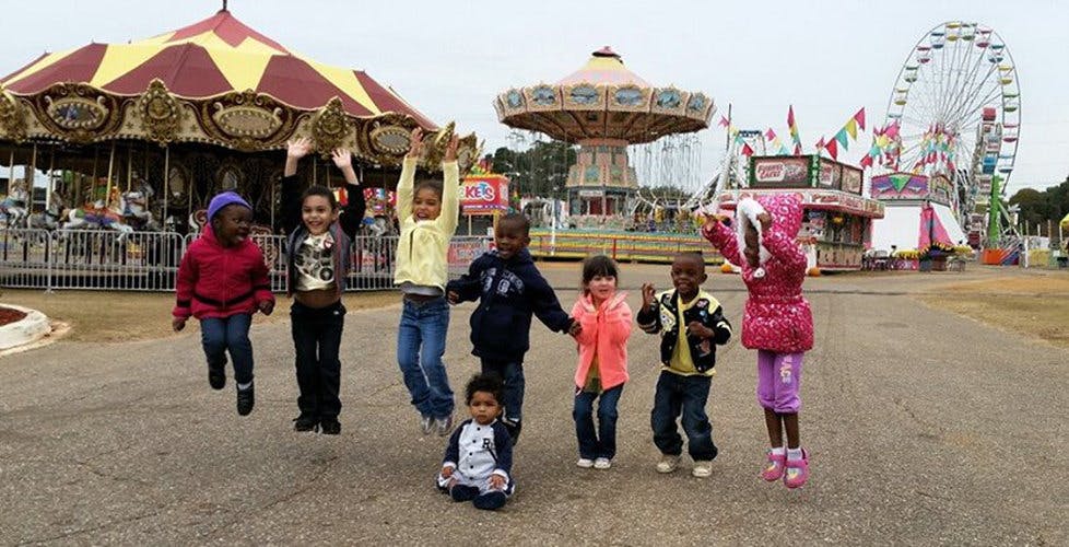 Children jumping in front of carnival rides