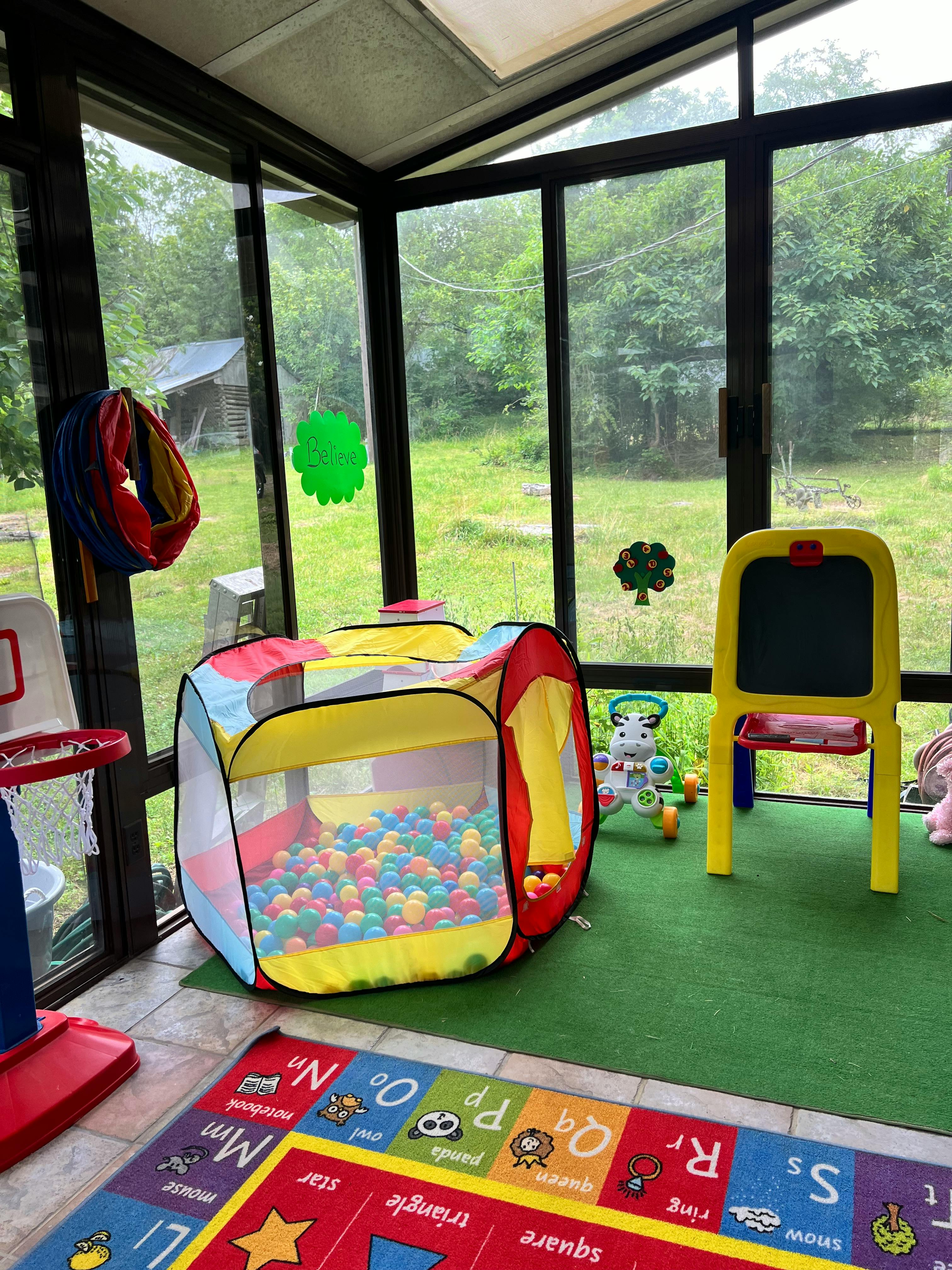 Indoor play area with a ball pit, easel, and alphabet rug