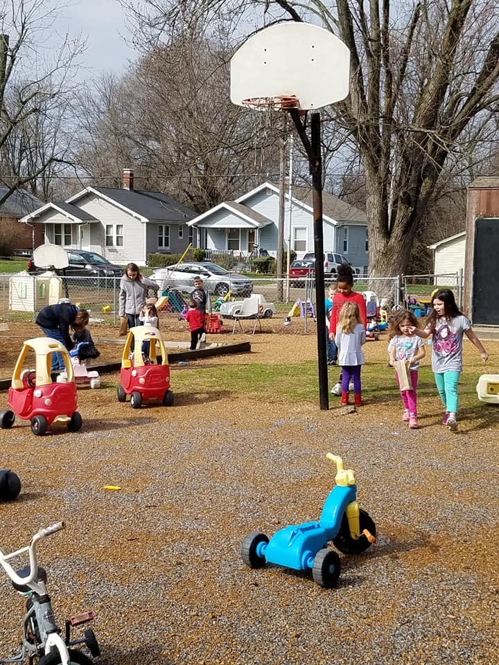 Children and adults on a playground with toy cars and a basketball hoop