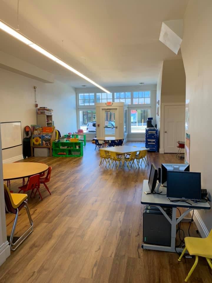 Empty classroom with small tables and chairs, computers, and large windows