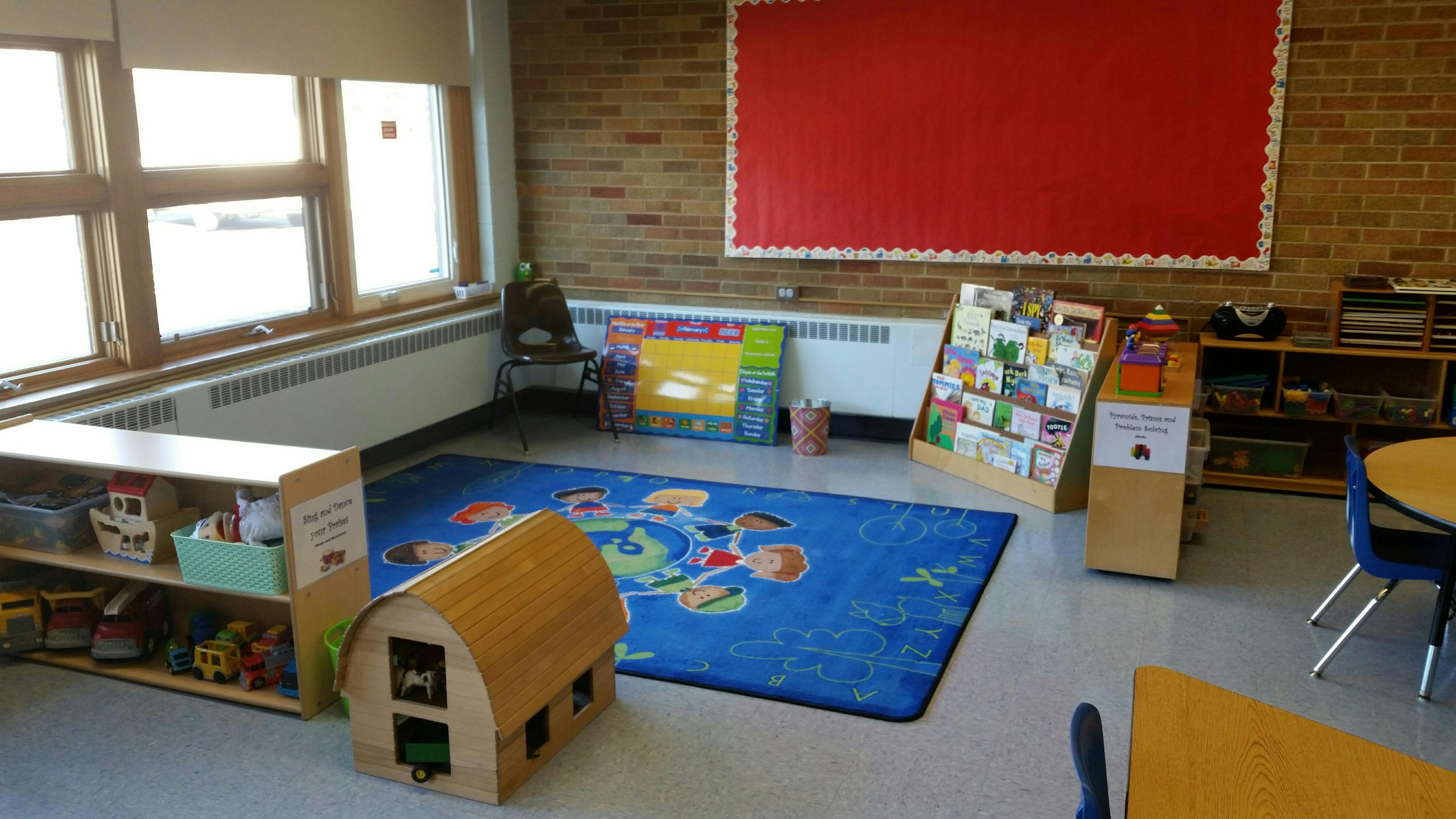 Classroom with a blue rug, wooden shelves, and a red bulletin board