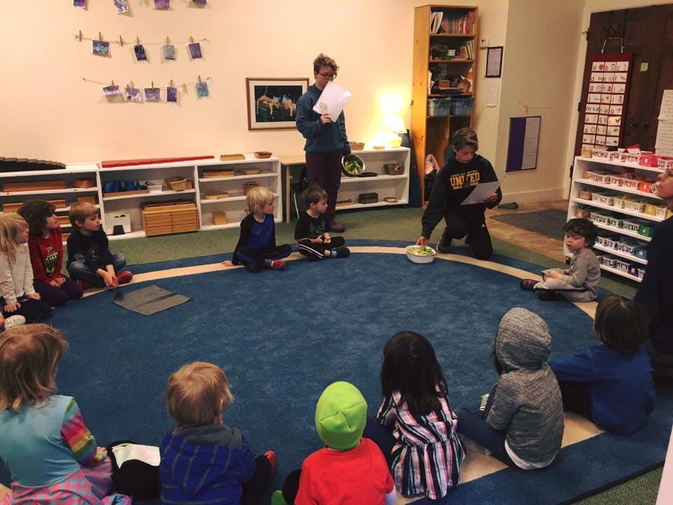 Adults and children sitting in a circle on a blue rug in a classroom