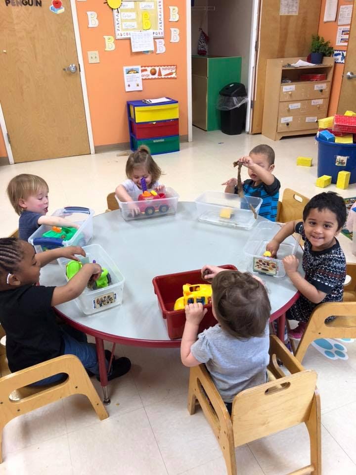 Children playing with toys around a table in a classroom
