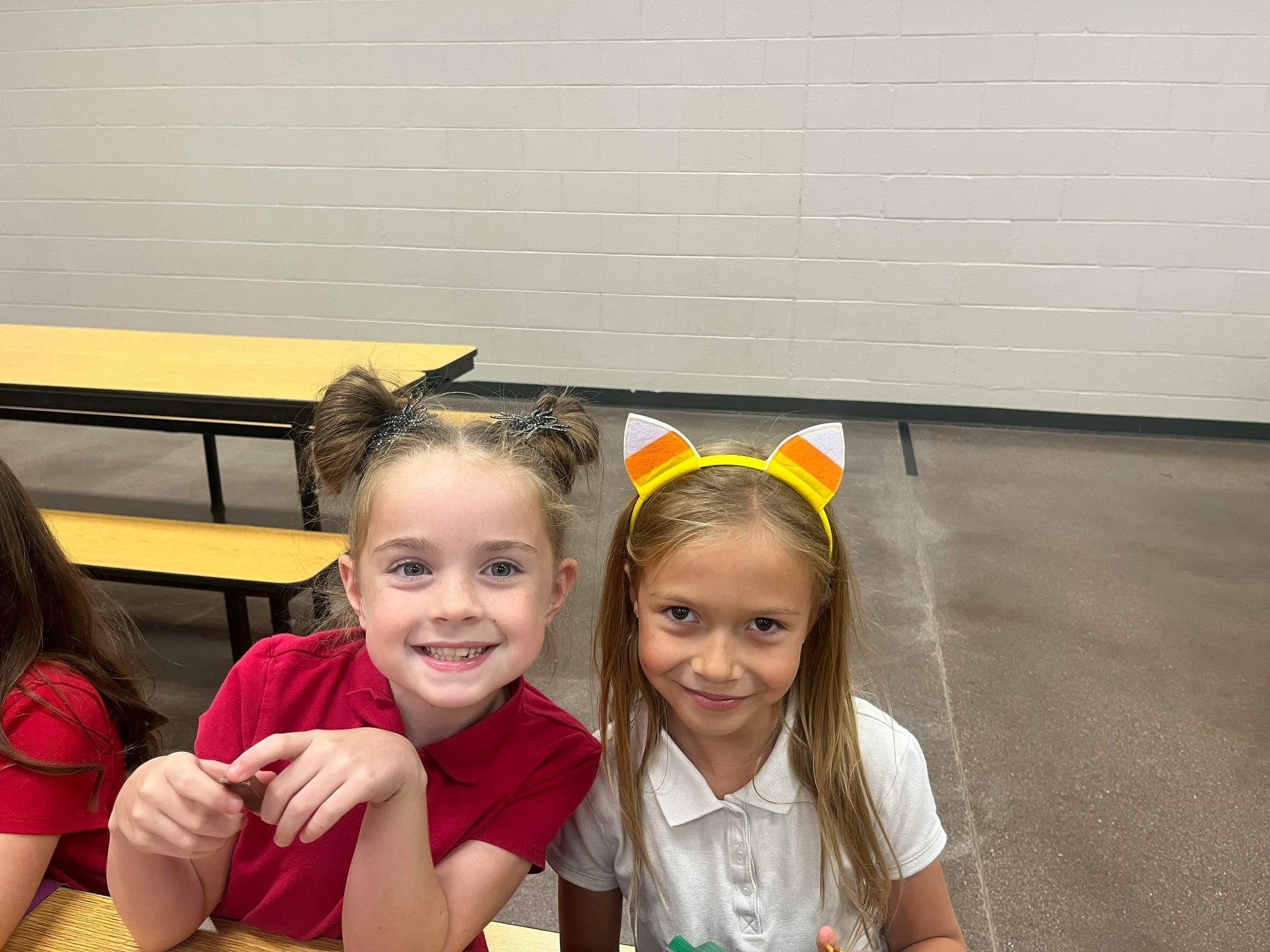 Two children smiling, one wearing a candy corn headband