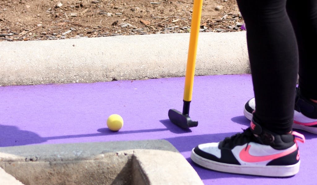 Person playing mini golf with a yellow ball and putter