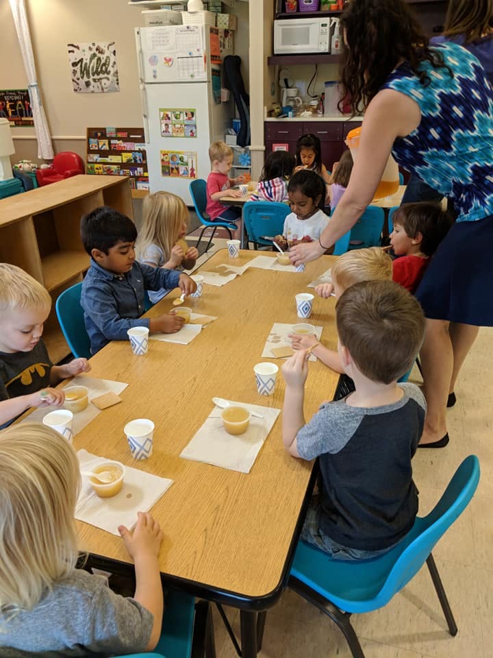 Adult helping children at a table in a classroom