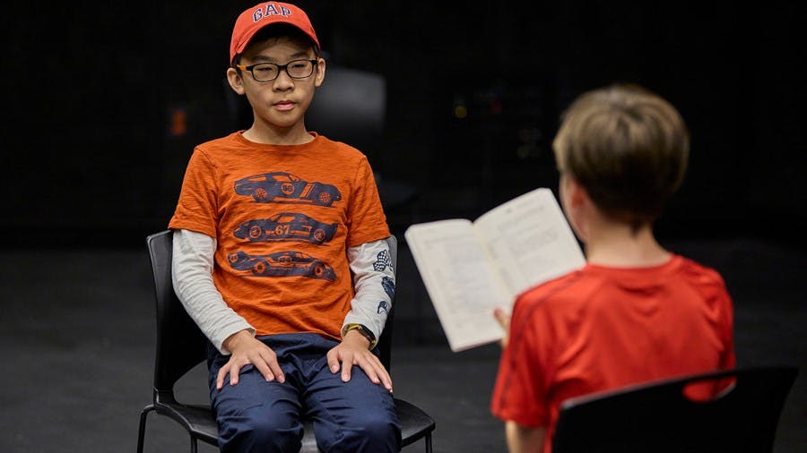Child in red hat and orange shirt sitting and looking forward