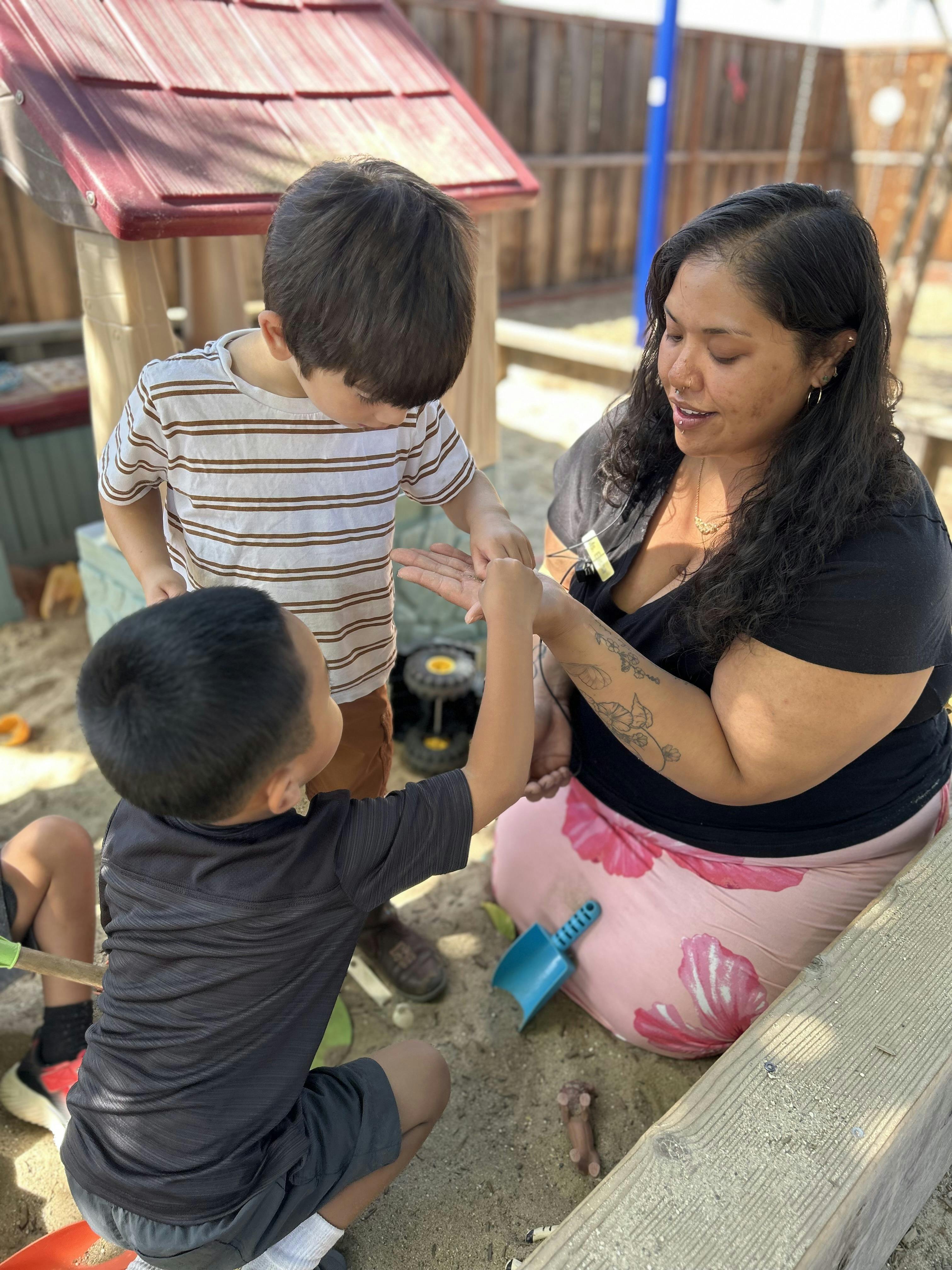 Adult and two children playing with sand in a sandbox