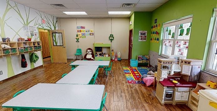 Empty classroom with small tables and chairs, play kitchen, and colorful rug