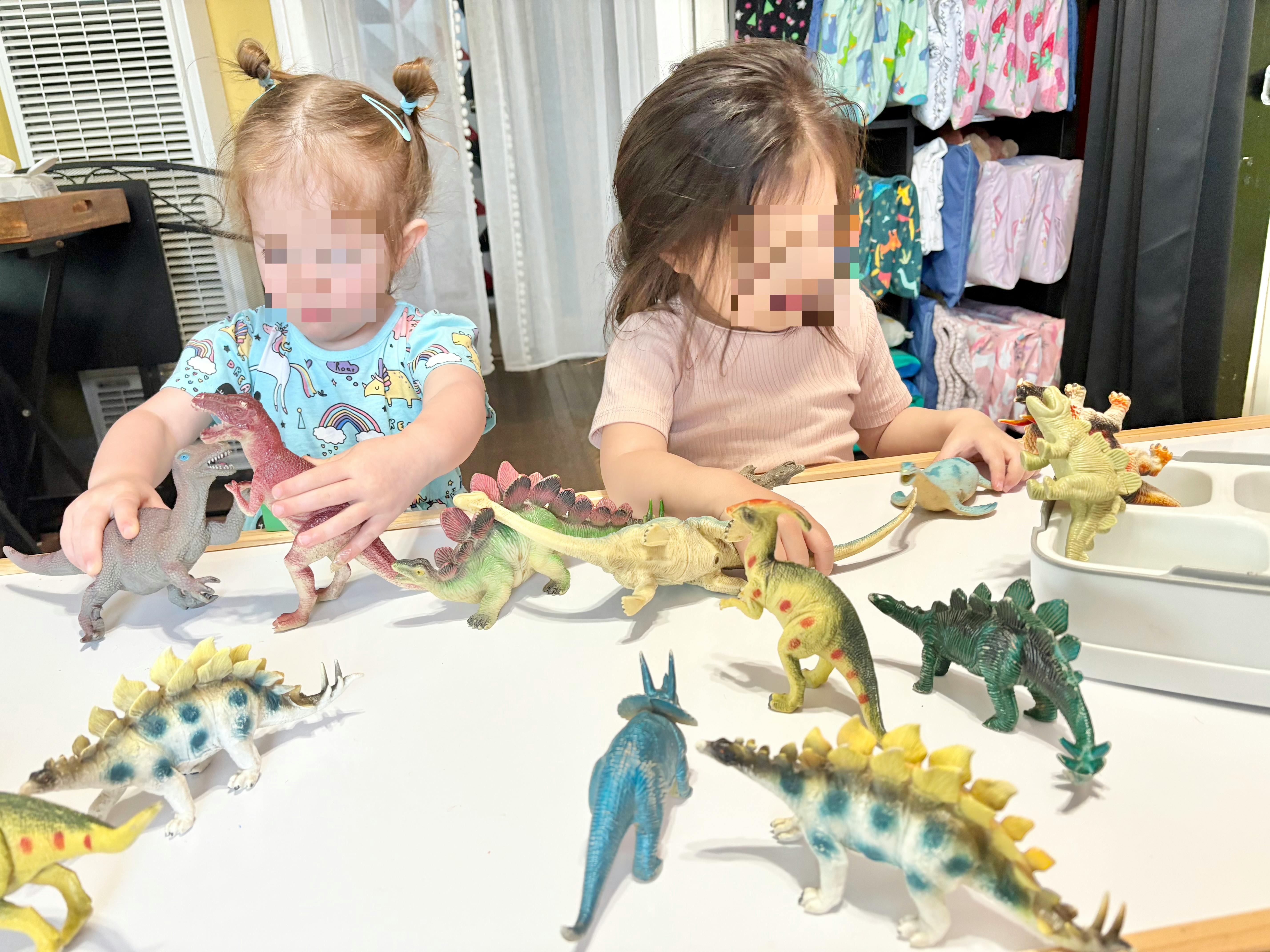 Two children playing with dinosaur toys on a table