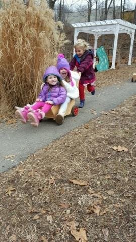 Three children playing with a wooden wagon outdoors