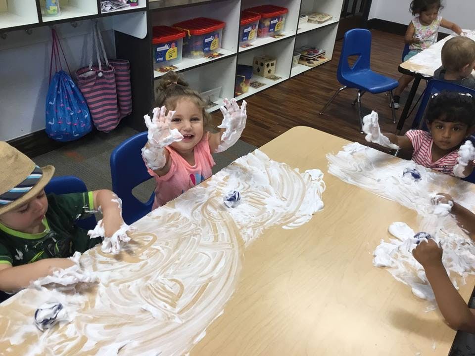 Children playing with shaving cream on a table in a classroom