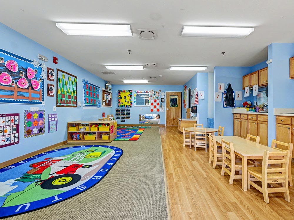 Classroom with blue walls, children's art, play rug, and small tables