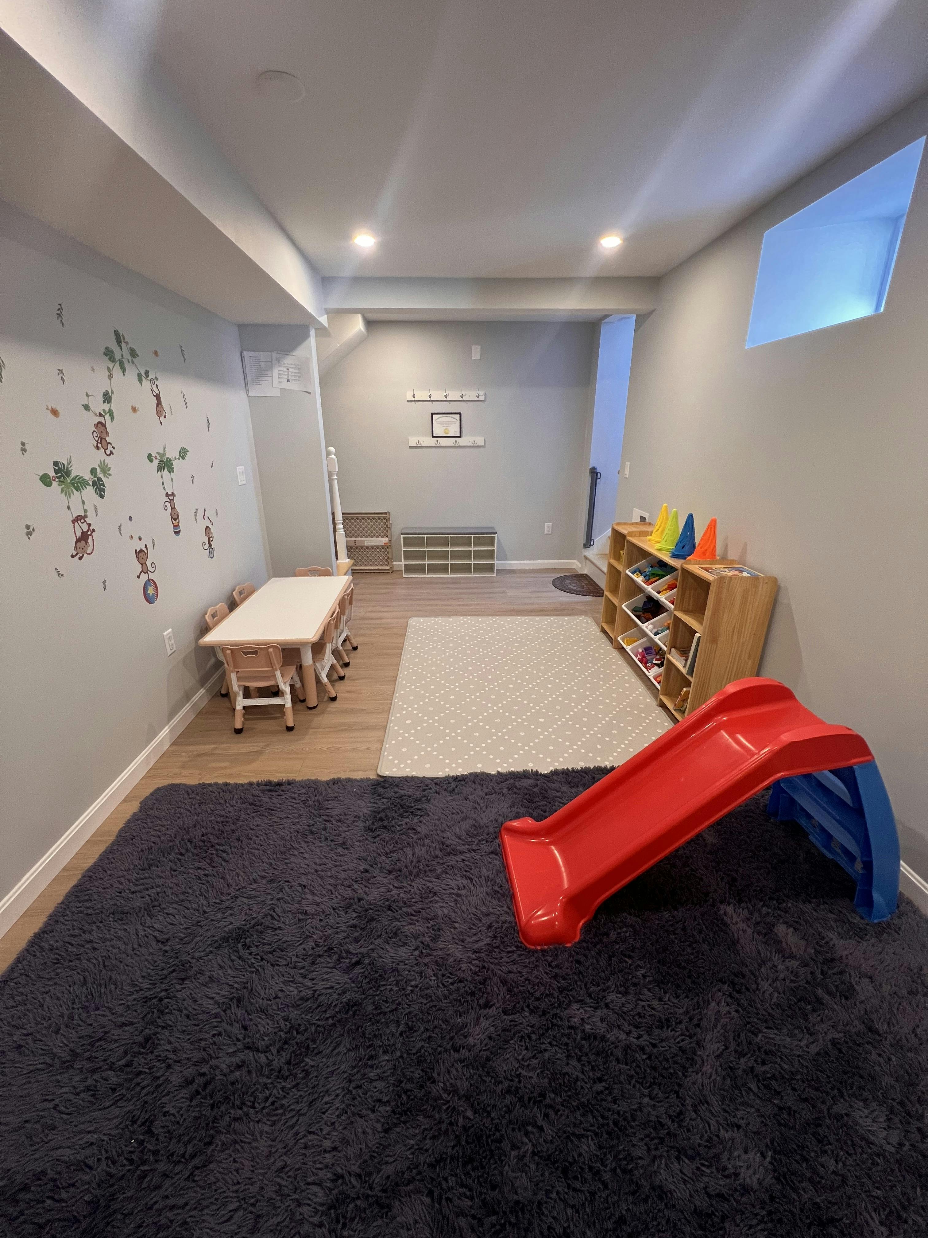 Playroom with a small red slide, child-sized table and chairs, and storage shelves