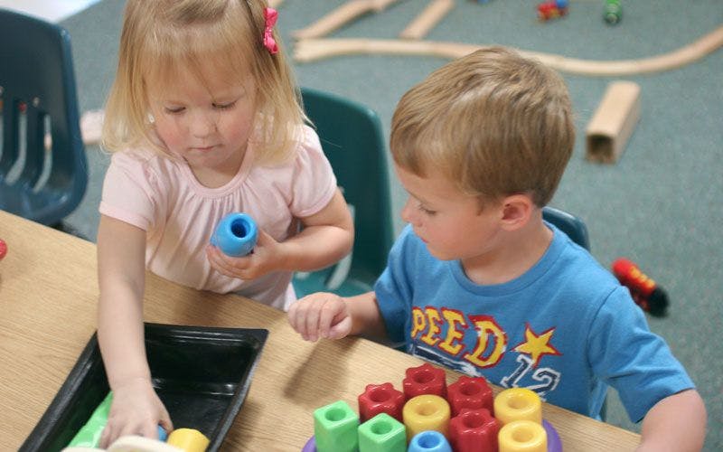 Two children playing with colorful blocks at a table