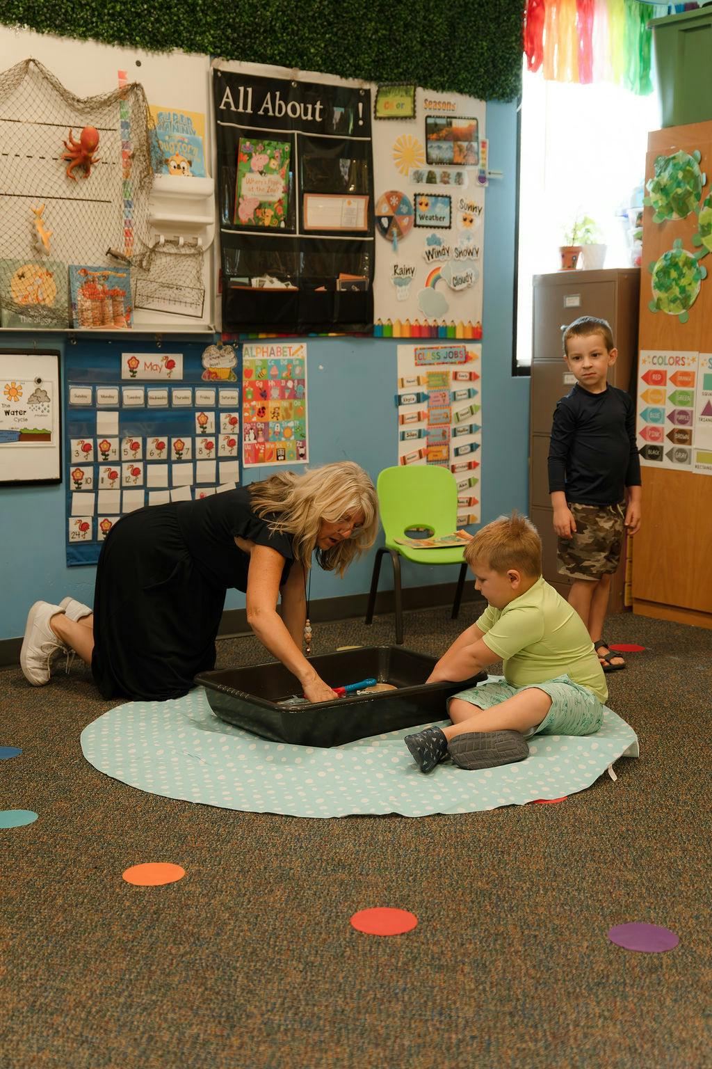 Adult and child using a sensory bin on a mat in a classroom