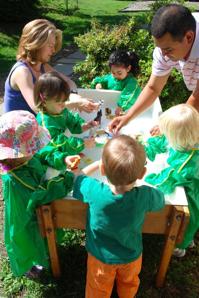 Two adults and multiple children playing at a water table outdoors
