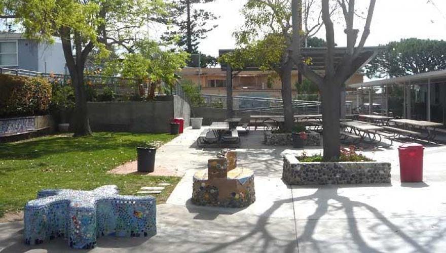 Outdoor area with trees, picnic tables, and a mosaic bench
