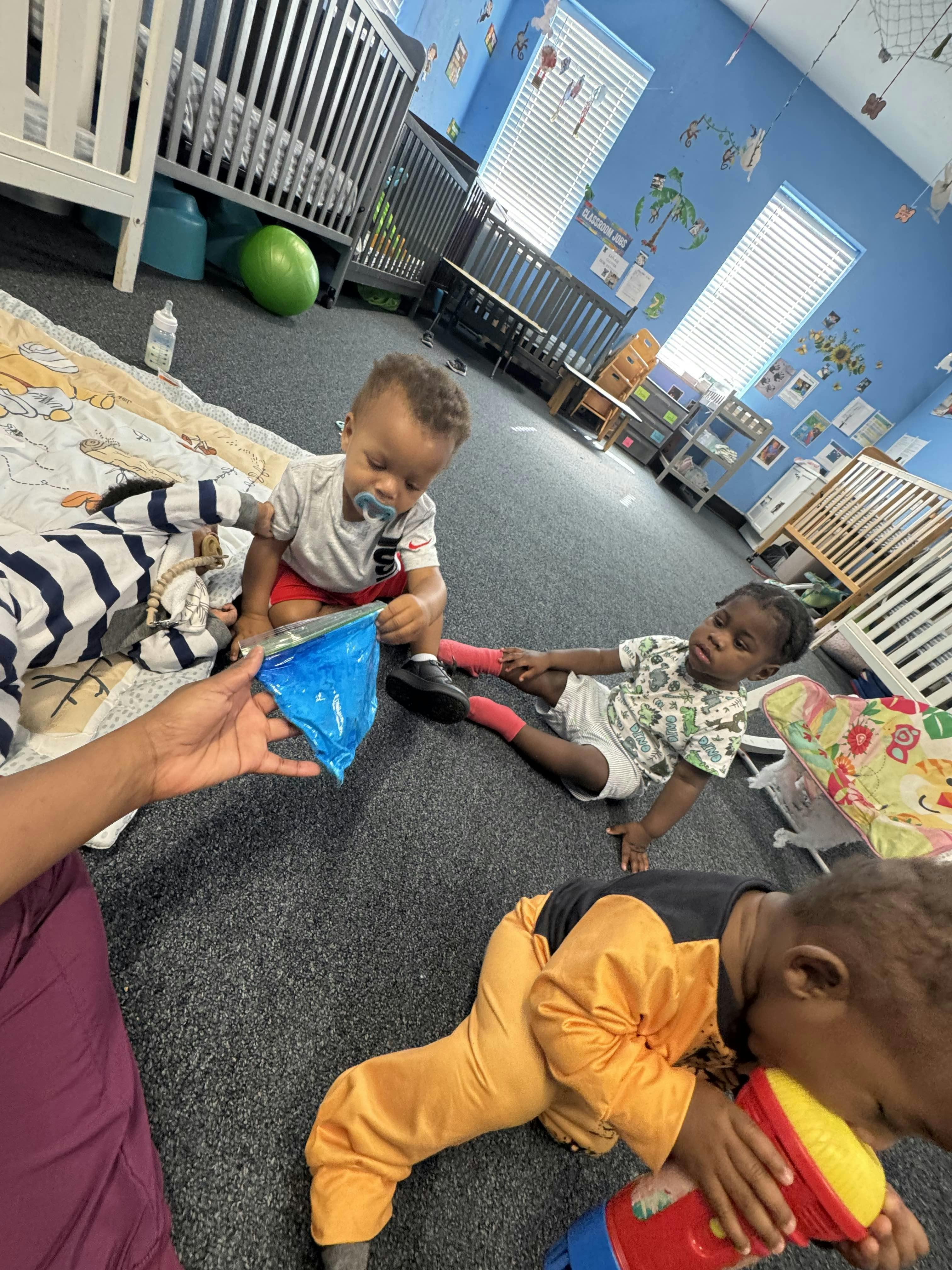 Three children playing on the floor in a room with cribs