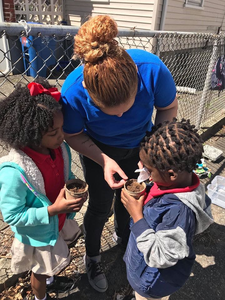 Person helping two children plant seeds in small pots