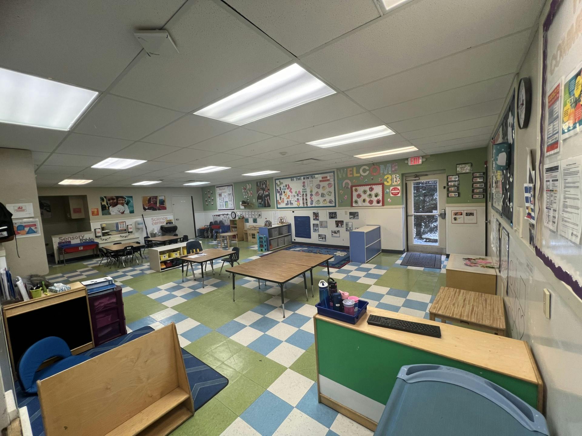 Empty classroom with checkered floor, small tables and chairs, and wall decorations