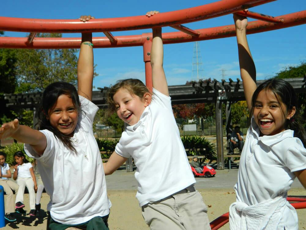 Three children hanging from monkey bars on a playground