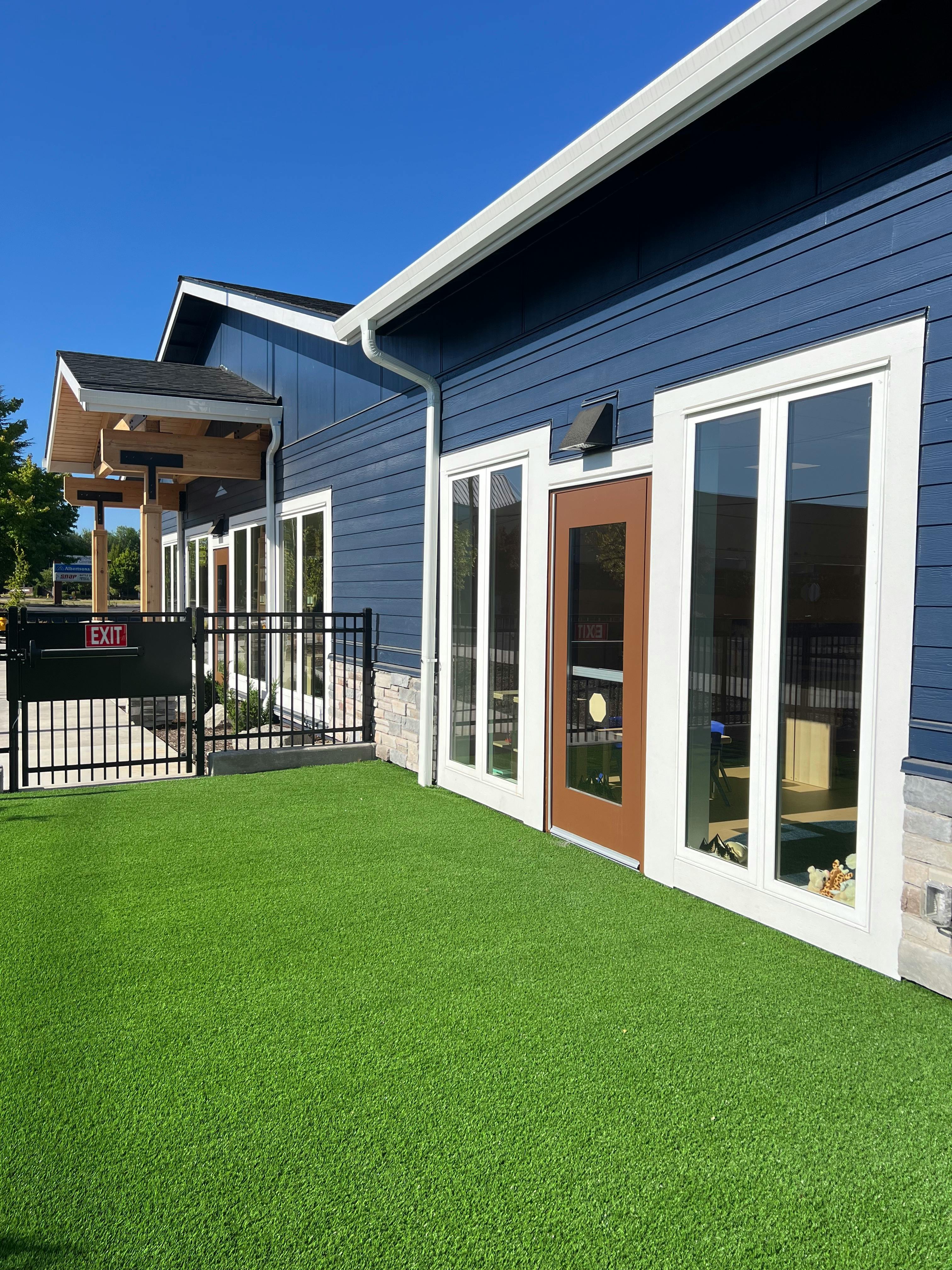 Blue building with white trim, brown door, and green artificial turf