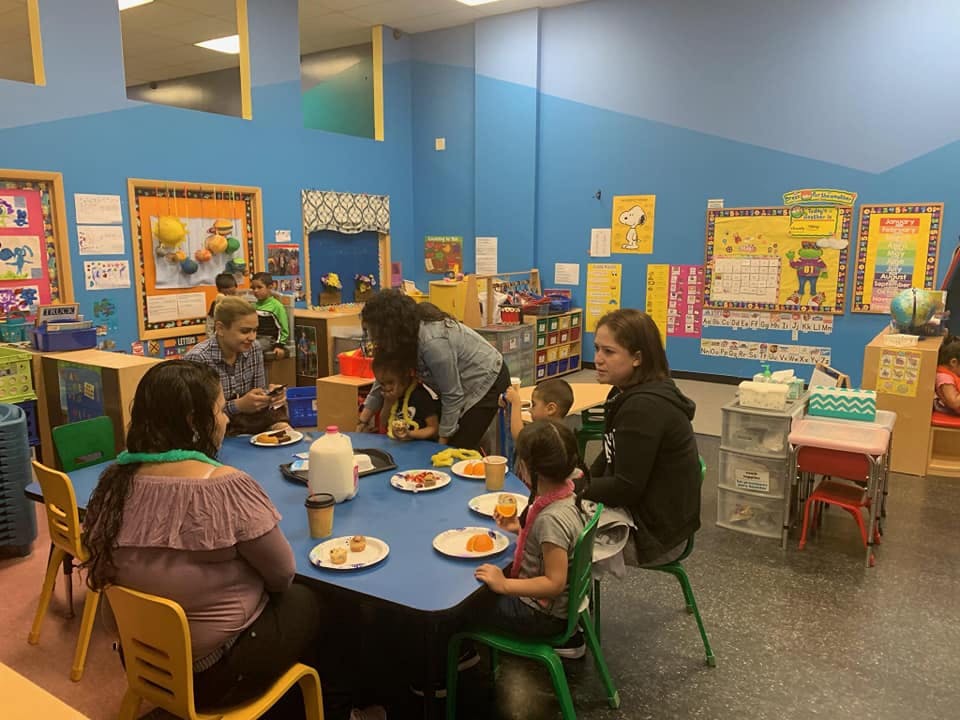 Adults and children sitting around a table with plates of food in a classroom