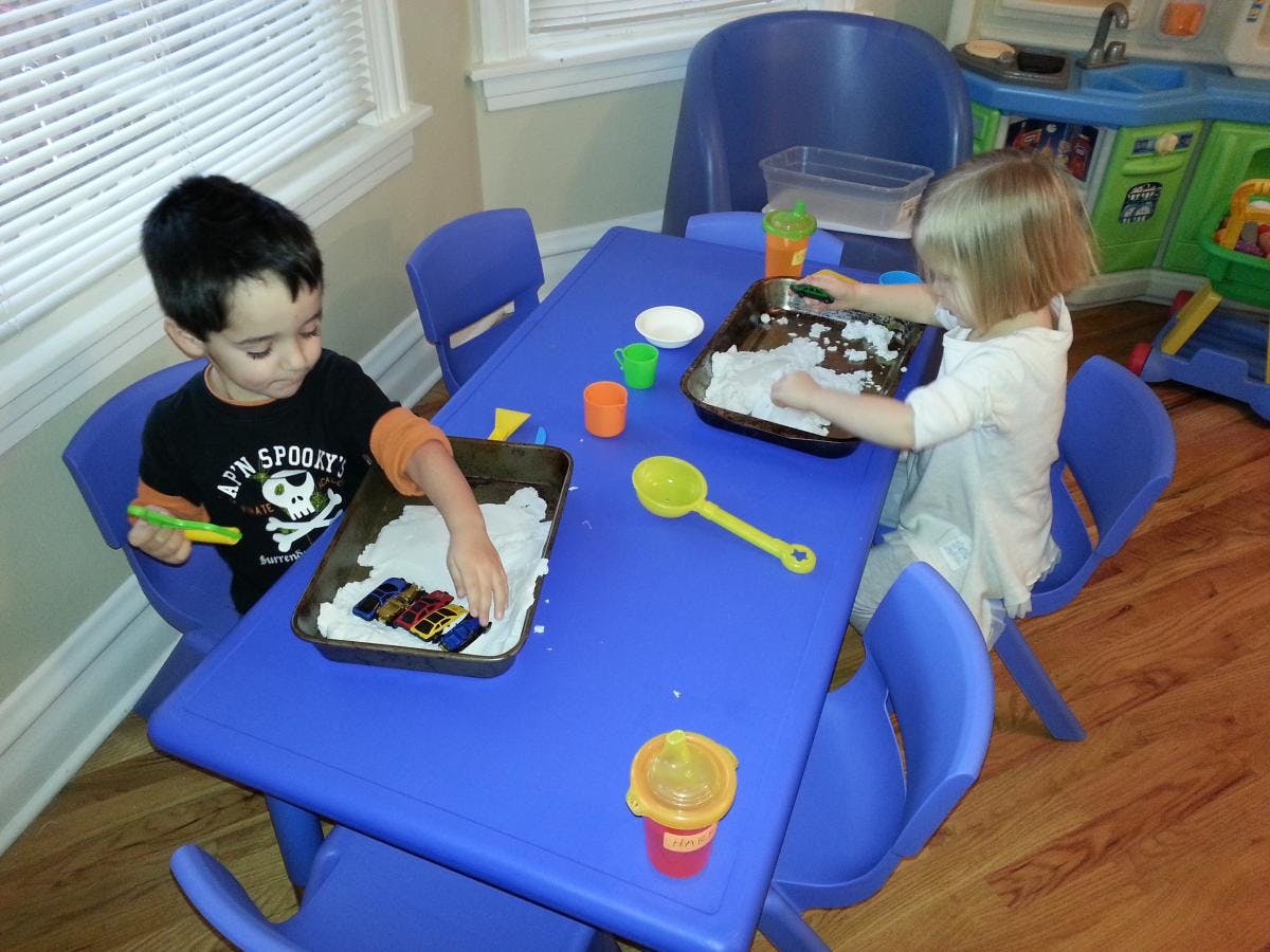 Two children playing with sensory bins at a blue table