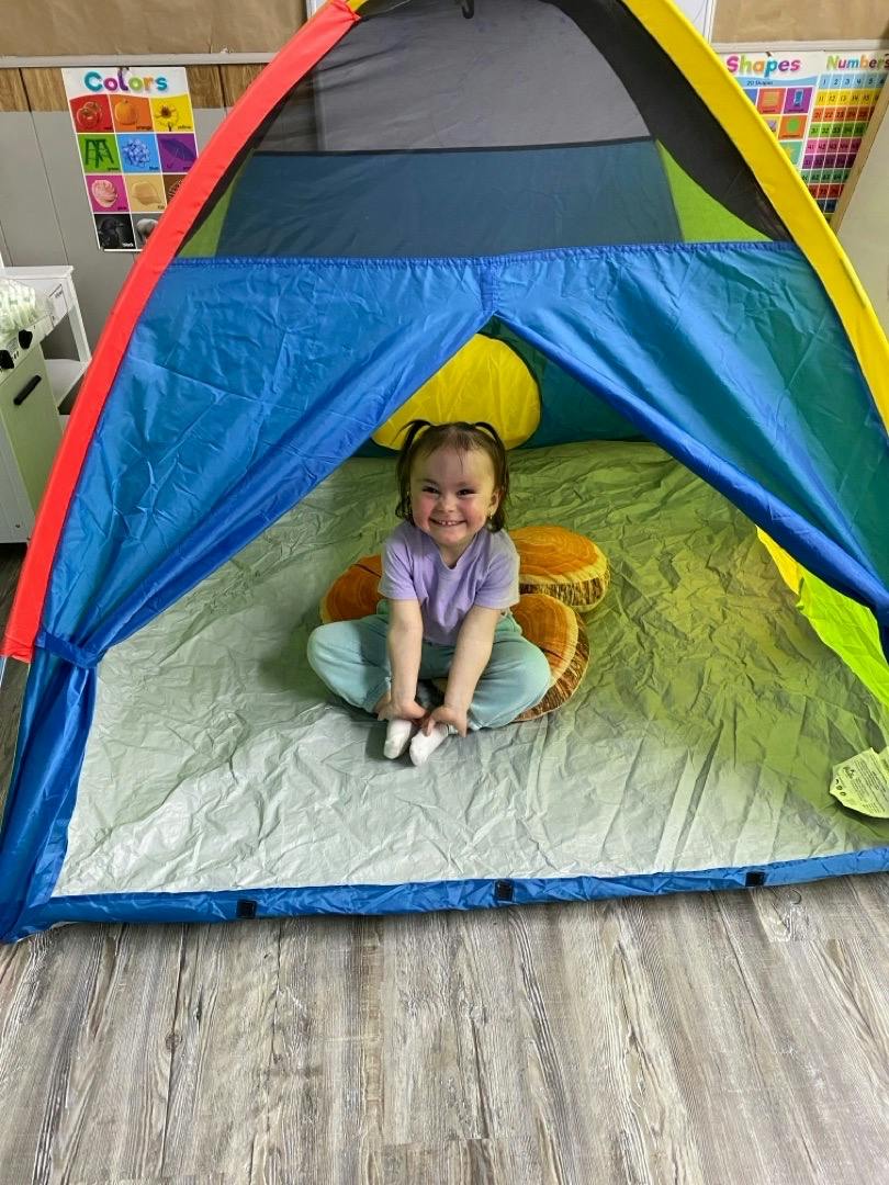 A child sitting inside a colorful play tent