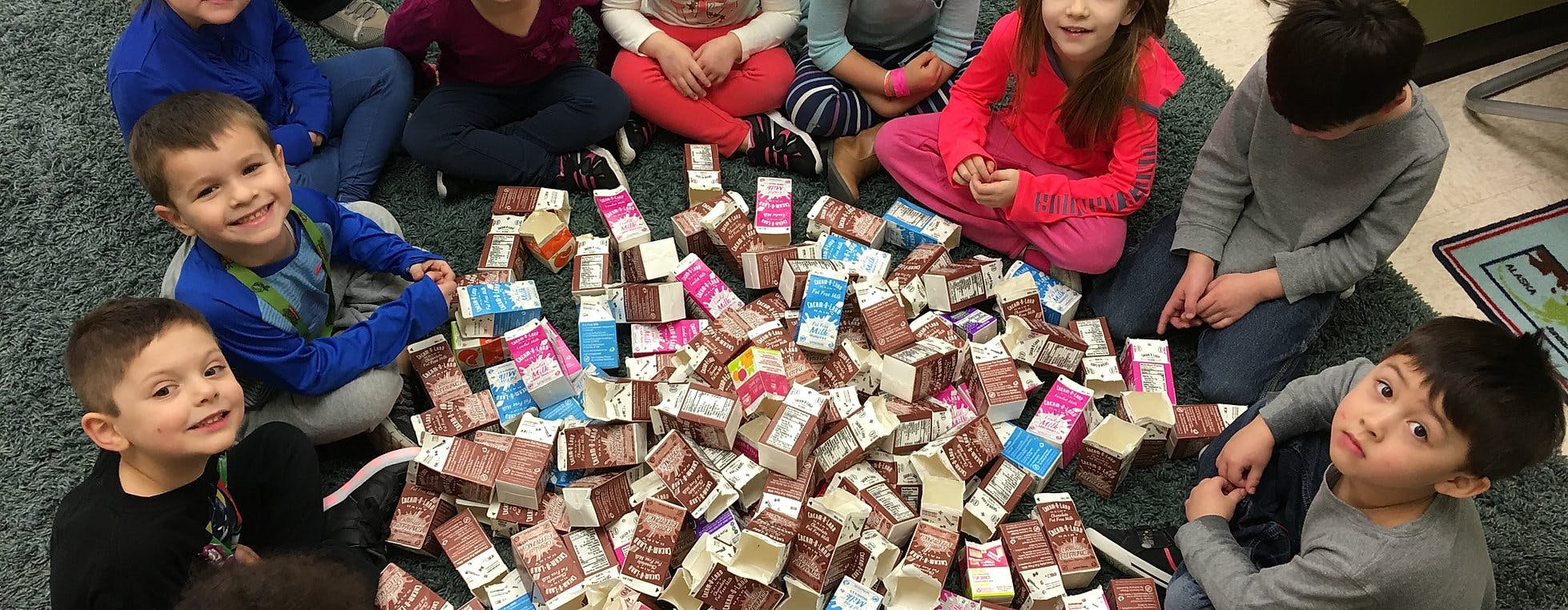 Children sitting around a large pile of small milk cartons