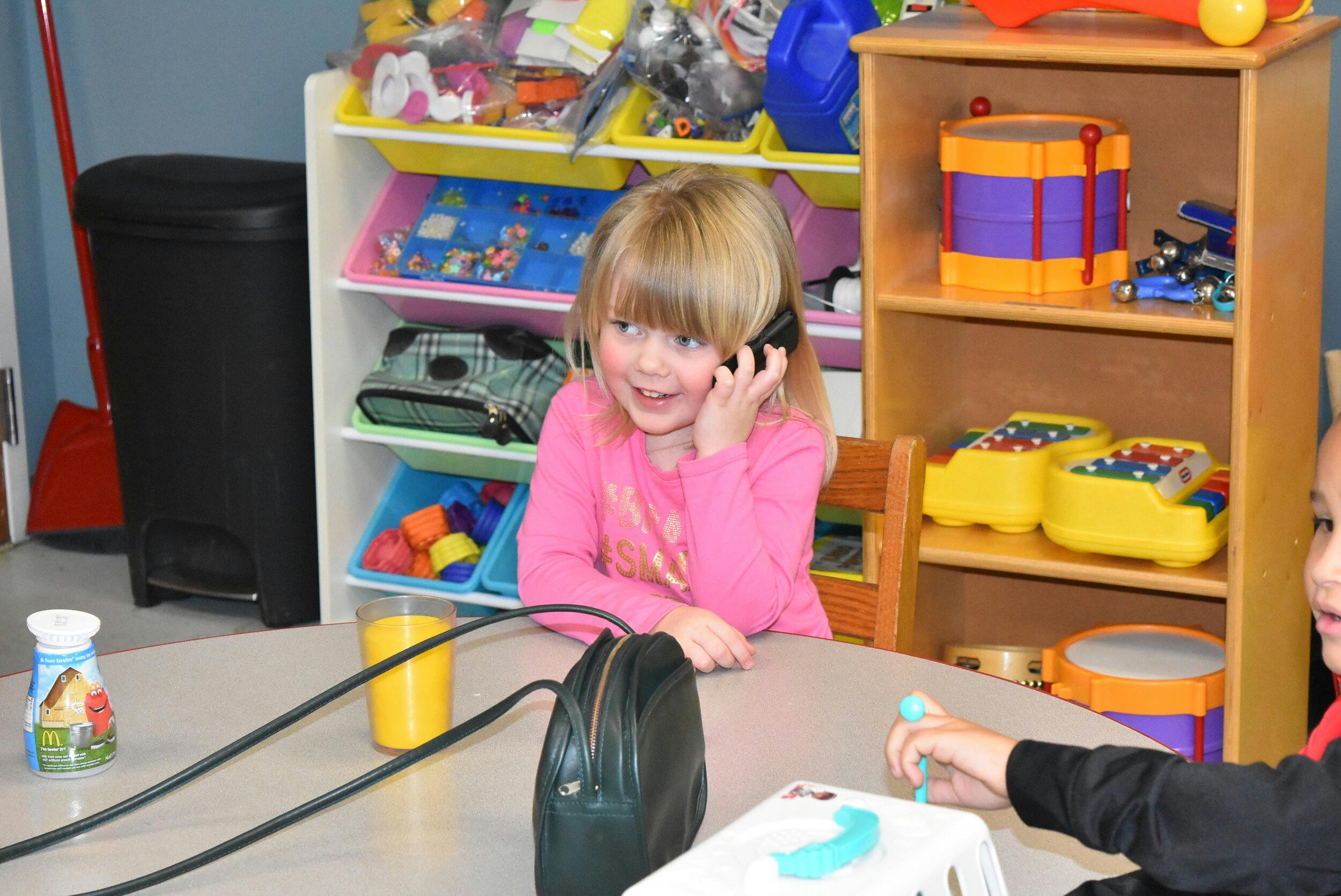 Child talking on a phone at a table in a classroom