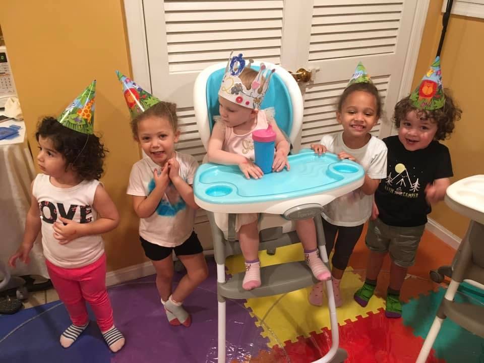 Four children wearing party hats, one child in a high chair