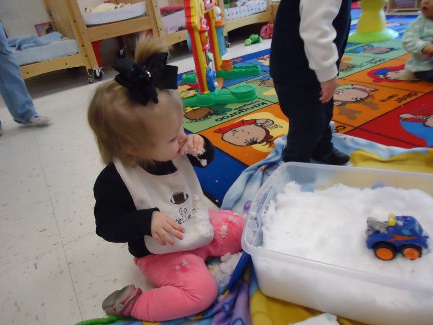 Child in a bib sitting on the floor next to a bin of white material and a toy truck
