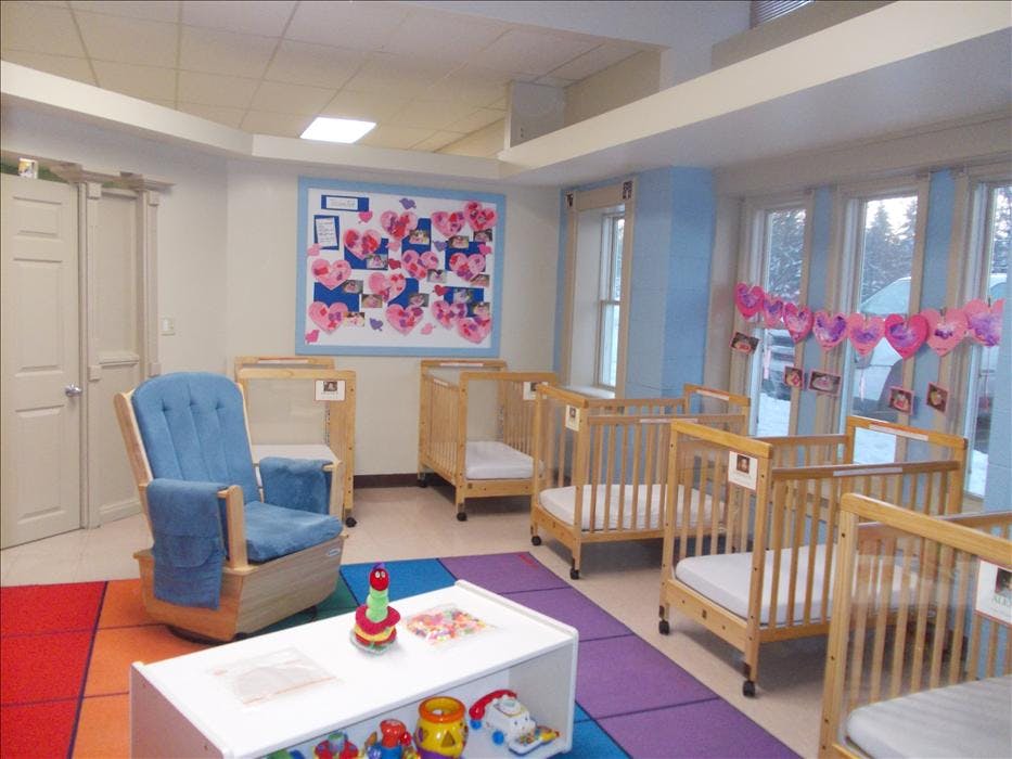 A room with multiple baby cribs, a blue rocking chair, and a colorful rug