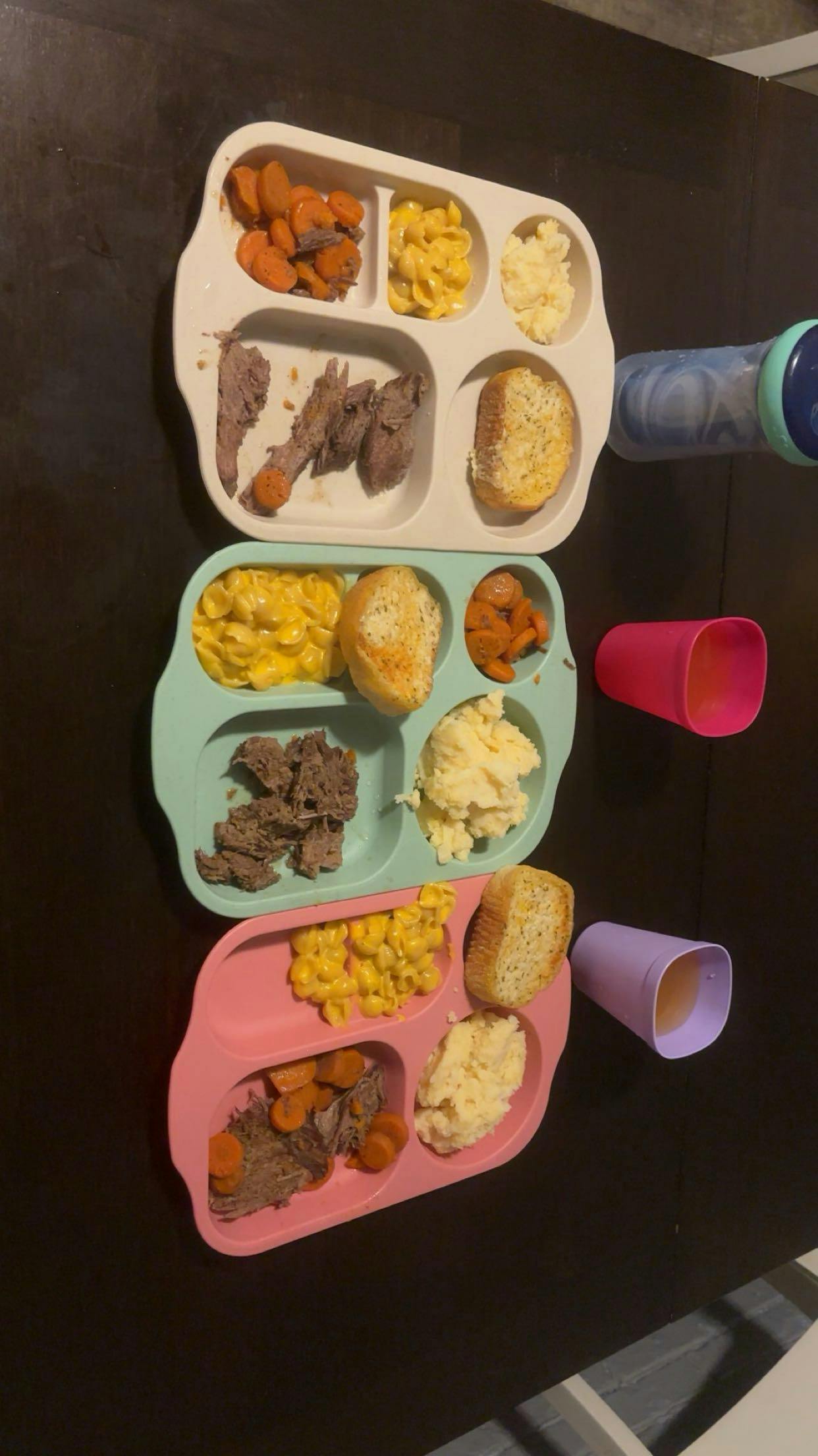 Three divided plates with portions of meat, macaroni, mash, carrots, and bread