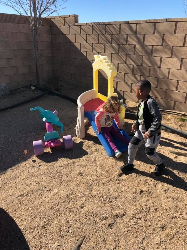 Two children playing on a small slide and toy in a dirt yard